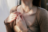 Person wearing a brown sweater adjusting a necklace with a blurred background